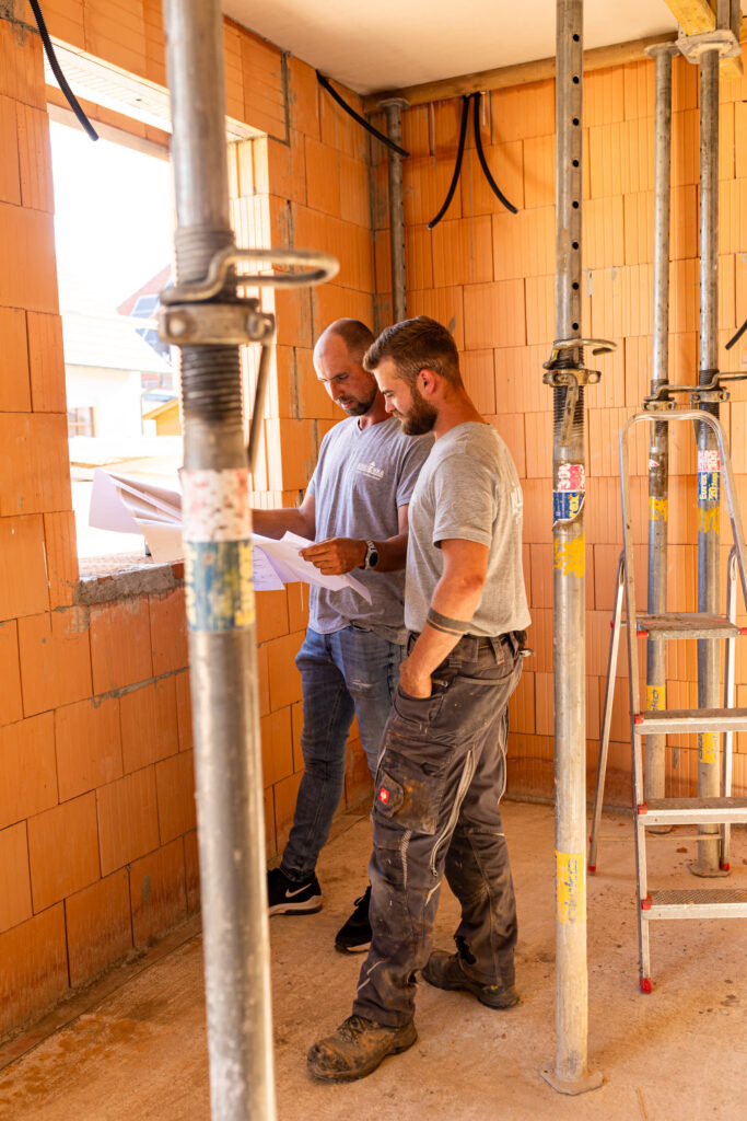 Zwei Mitarbeiter der Kauschka Hoch-Tiefbau GmbH besprechen den Bauplan im Rohbau